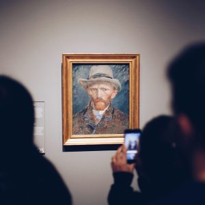 person taking picture of man wearing brown hat painting