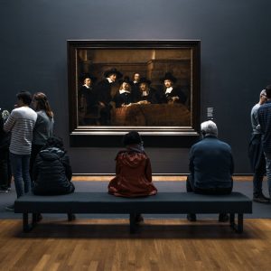 a group of people standing around a museum looking at a painting